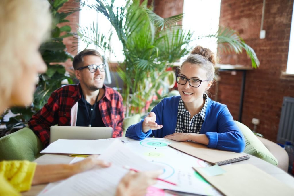 A man and a woman in glasses discussing charts at a table in a bright, plant-filled office, planning how to budget with irregular income