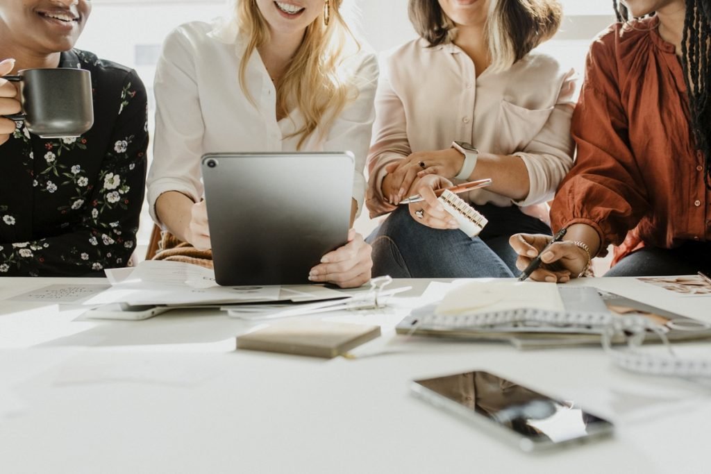 Four women gathered around a white table with a tablet, notebooks and coffee