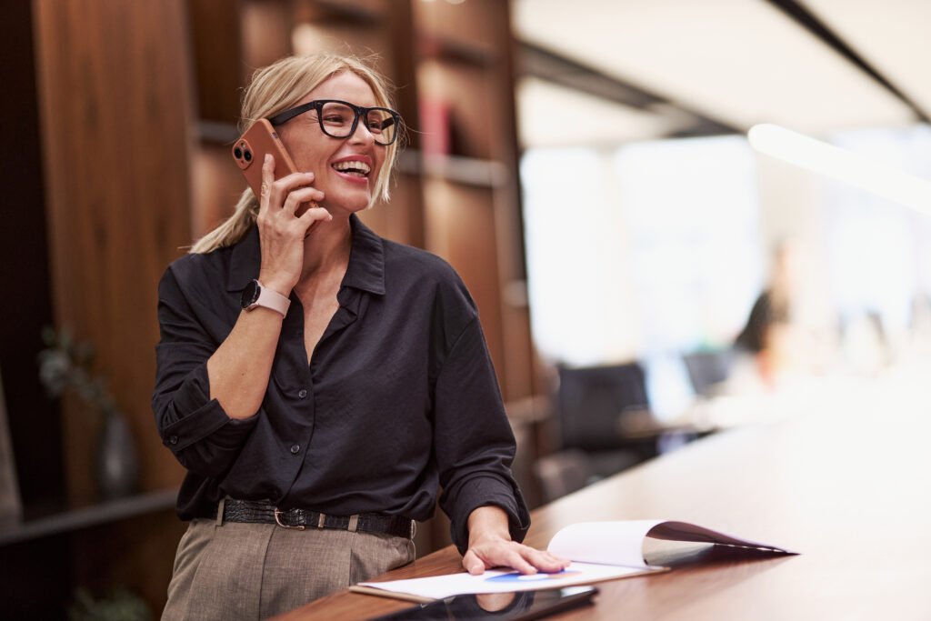 Smiling blonde woman in glasses talking on her phone in an office
