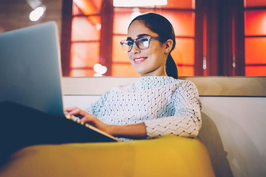 Woman in glasses working on a laptop in a yellow chair, setting up passive income streams.