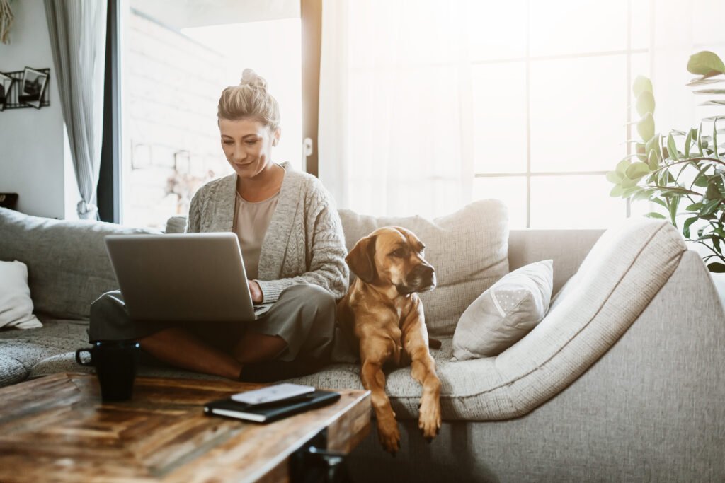 Woman on a couch with a dog and laptop