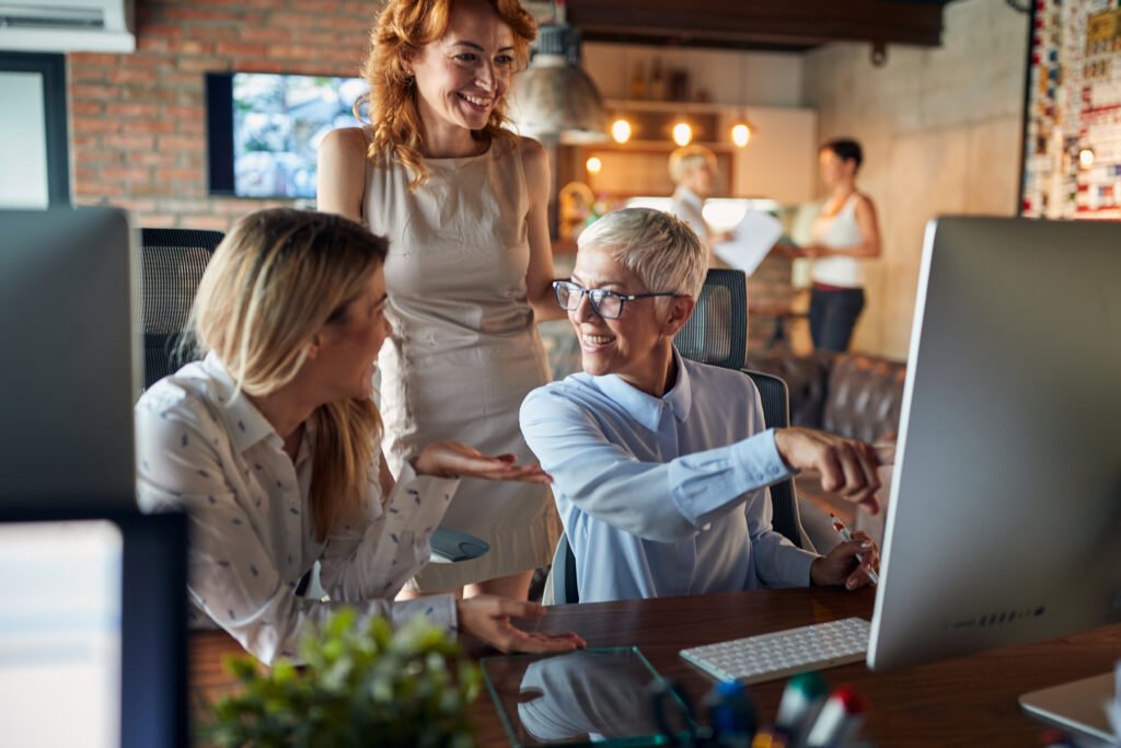 Smiling older woman showing two colleagues something on a computer screen