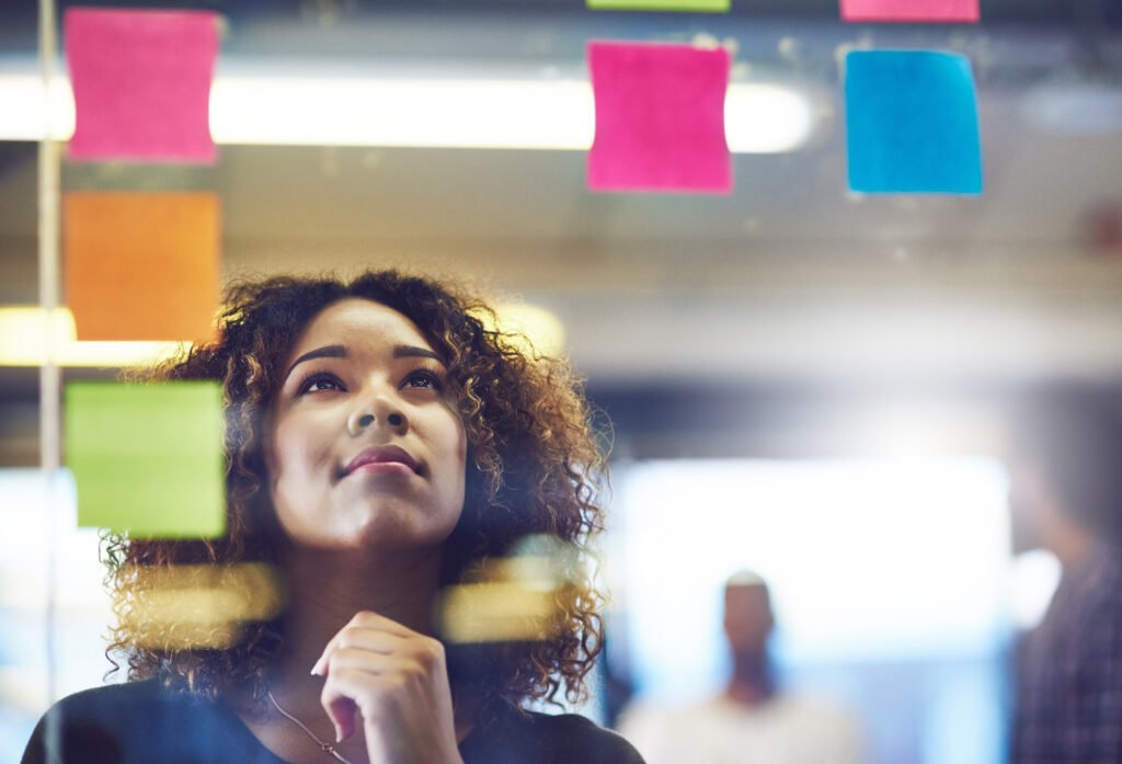Woman looking up thoughtfully at colorful sticky notes on a glass wall
