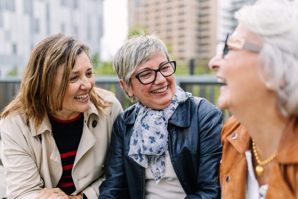 Three older women laughing together outdoors in the city