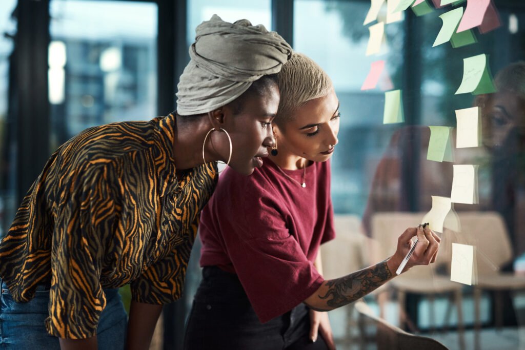 Two women adding sticky notes to a glass wall while planning