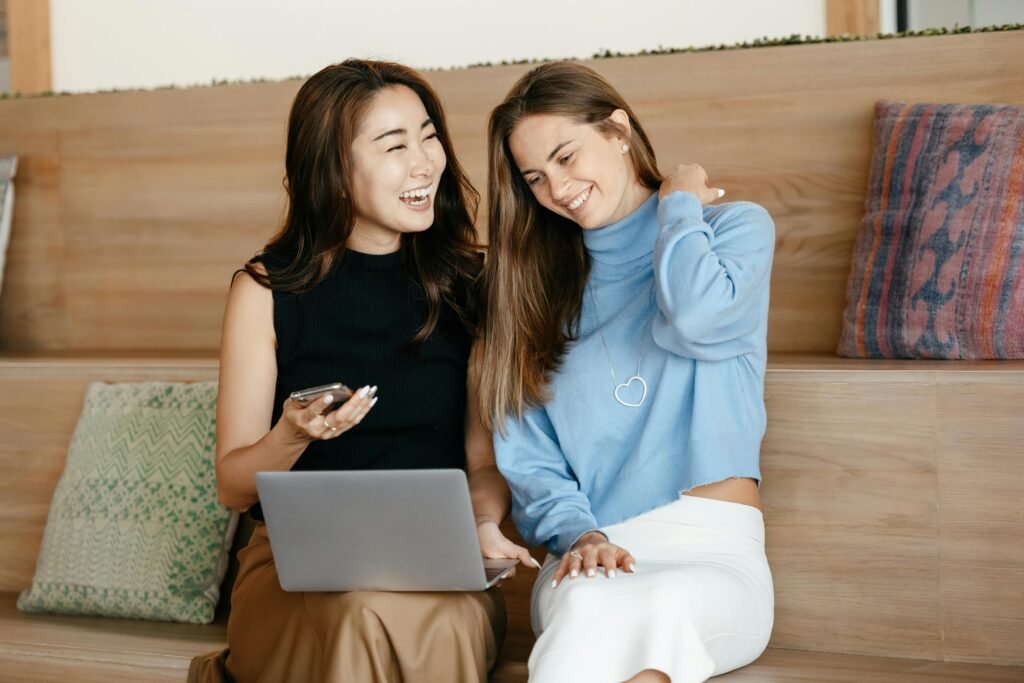 Two women on a couch with a laptop and phone, working out how to stop living paycheck to paycheck.