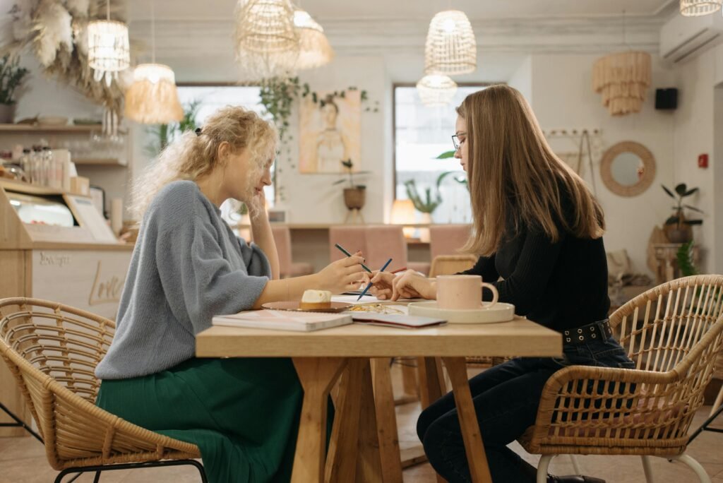 Two women working through notes across a small table in a boho café, checking for money leaks in business