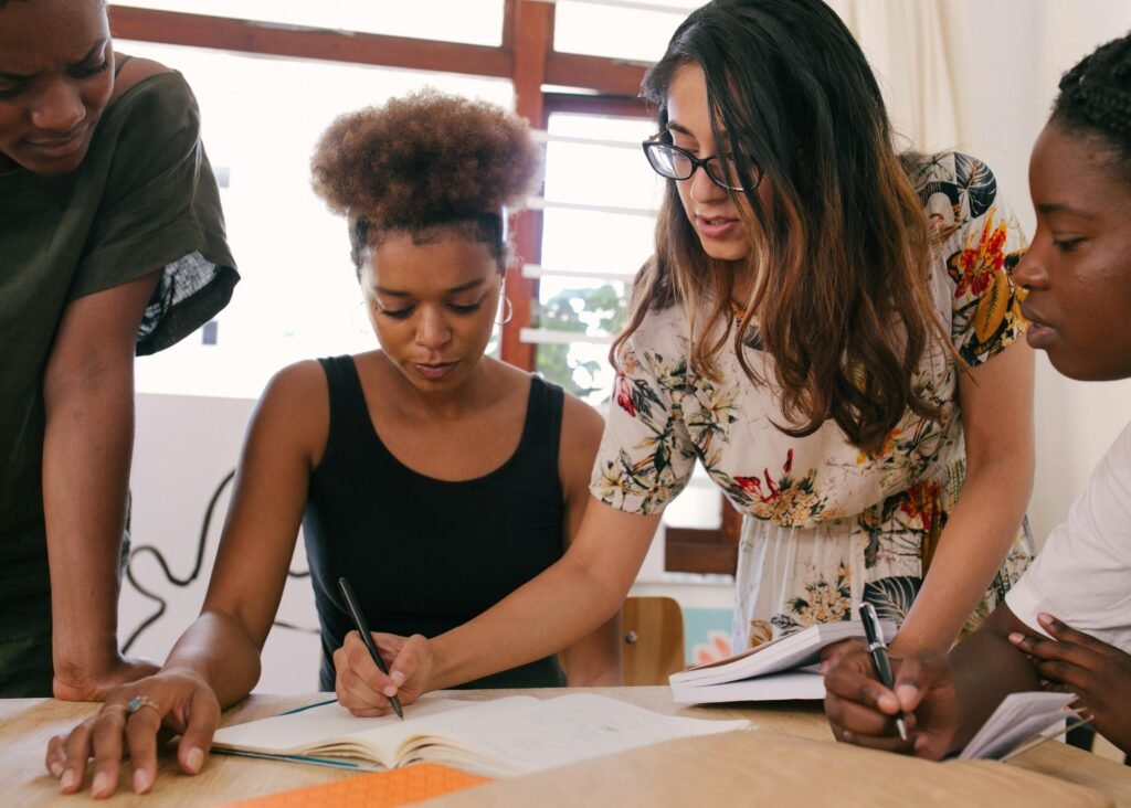 Young women gathered around a table, working through notes in a notebook together as they set up the Profit First method