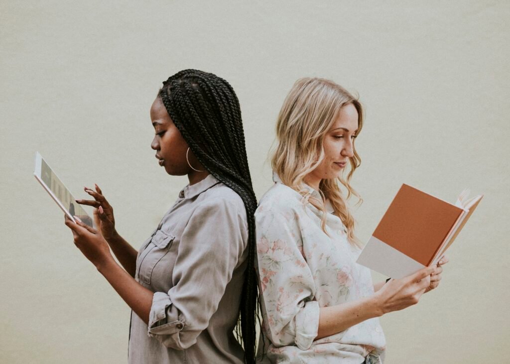 Two women standing back to back, one on a tablet and one reading a book, soaking up advice before signing up for another course