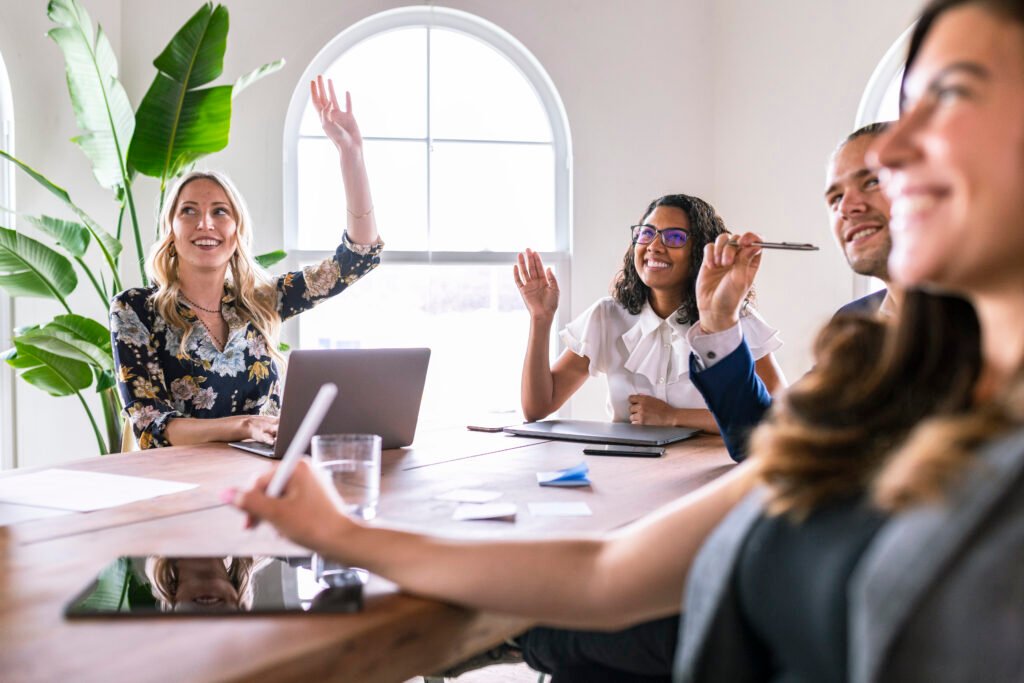 Team members raising their hands during a meeting around a conference table, owning up to financial mistakes small business owners make