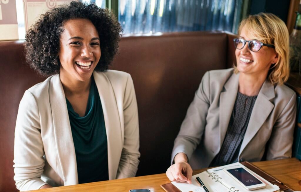 Two Black businesswomen talking on a sofa about how to rewire your money mindset.