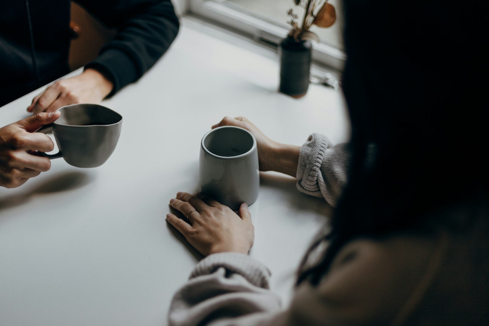Two people holding mugs across a table