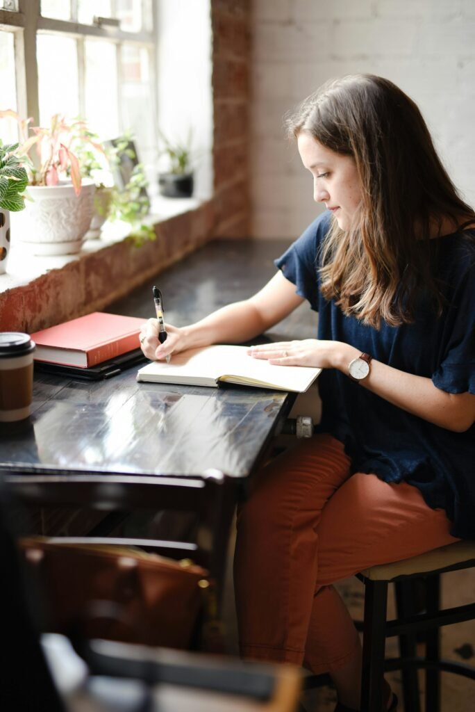 Woman writing in a notebook by a window