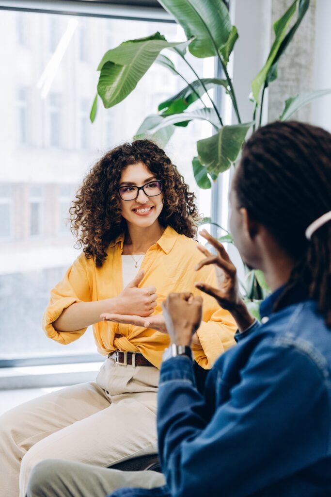 Two people talking in sign language in a bright room with a large plant