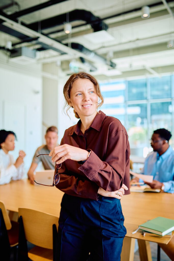 A smiling red haired woman standing in a busy office, ready to fix a website that isn't getting clients.