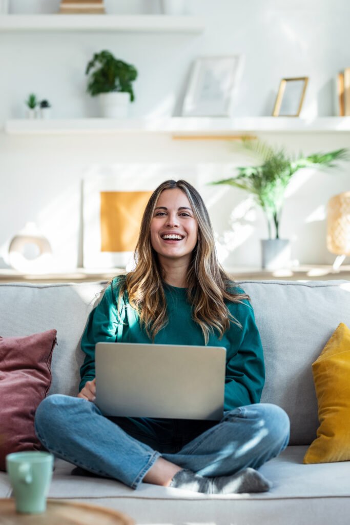 A woman smiling on her couch with a laptop