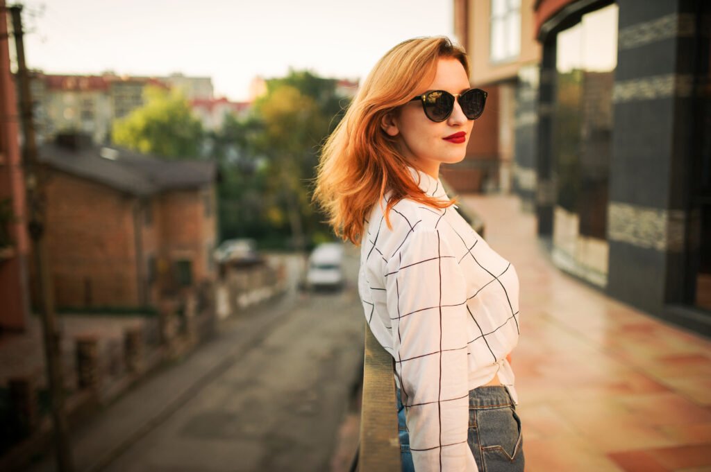 Red-haired woman in sunglasses on a city street, confident in the personal brand she chose to build
