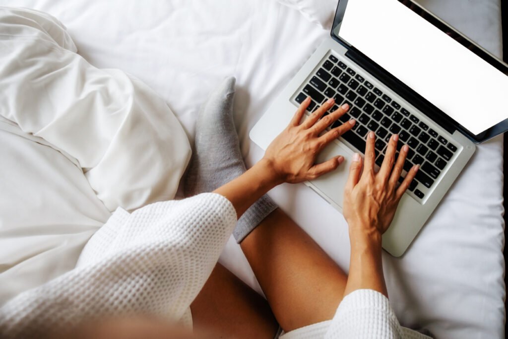 Hands typing on a laptop on a white bed