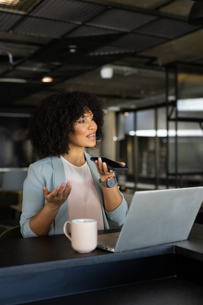 Woman in a light blue blazer speaking into her phone at her laptop, answering DMs to build an email list from Instagram