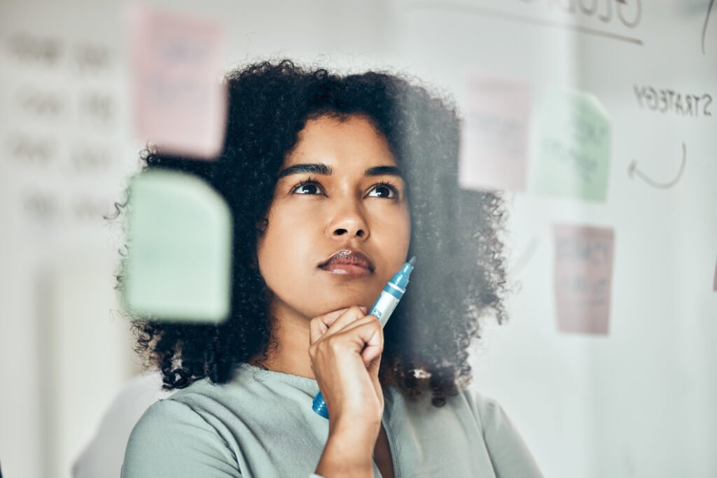 Woman with curly hair studying sticky notes on a glass board, planning how to make money on YouTube without ads