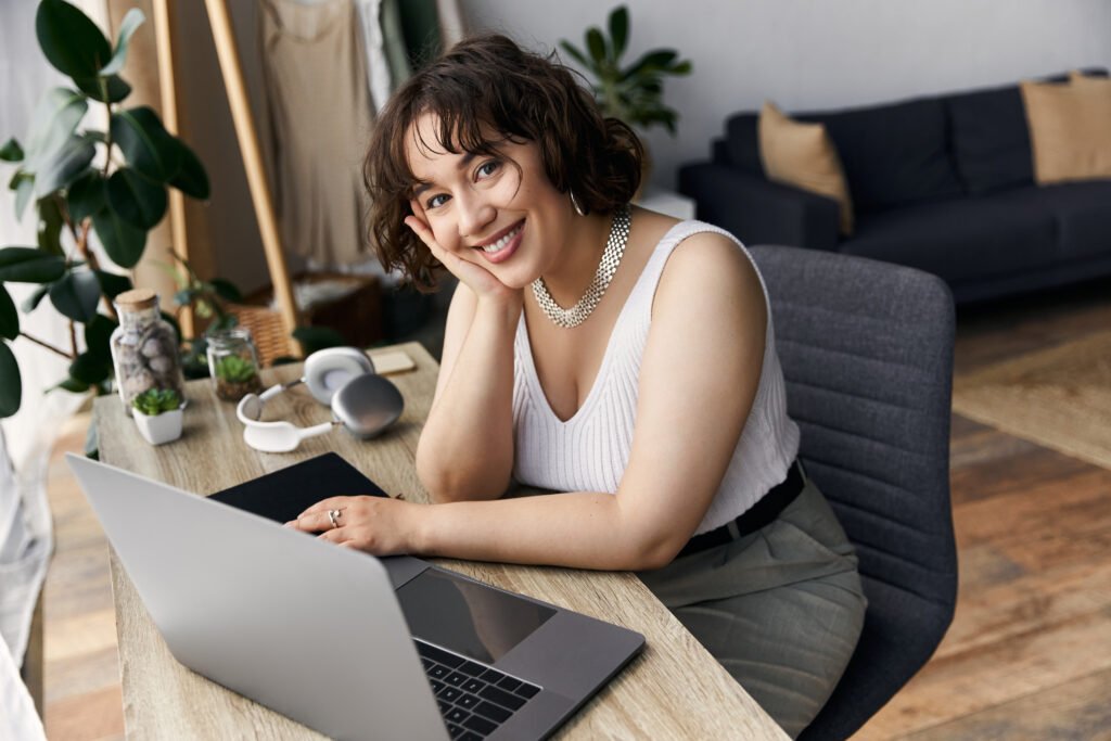 Smiling woman resting her chin on her hand at a wooden desk with a laptop